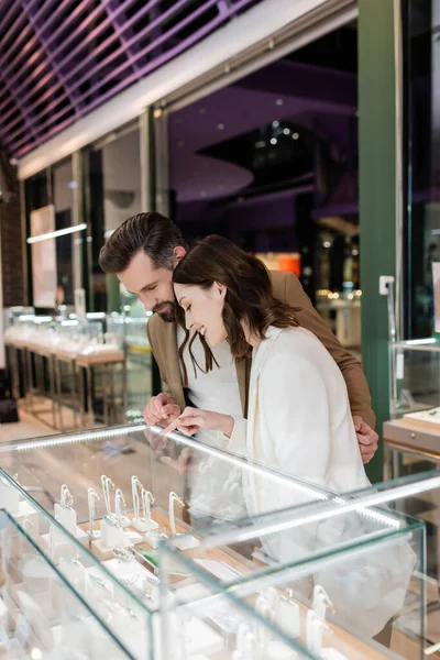 Man looking at showcase while girlfriend pointing with finger in jewelry shop