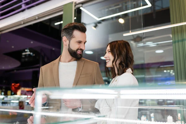 Smiling Man Pointing Showcase Looking Girlfriend Jewelry Shop — Stock Fotó