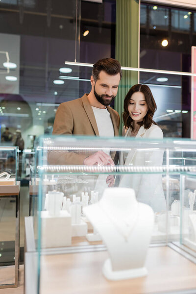 Bearded man pointing at jewelry in showcase near girlfriend in store 
