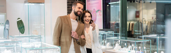Excited woman pointing at showcase near boyfriend in jewelry shop, banner 