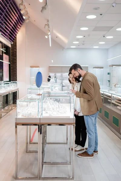 Customer pointing at jewelry near smiling girlfriend in shop