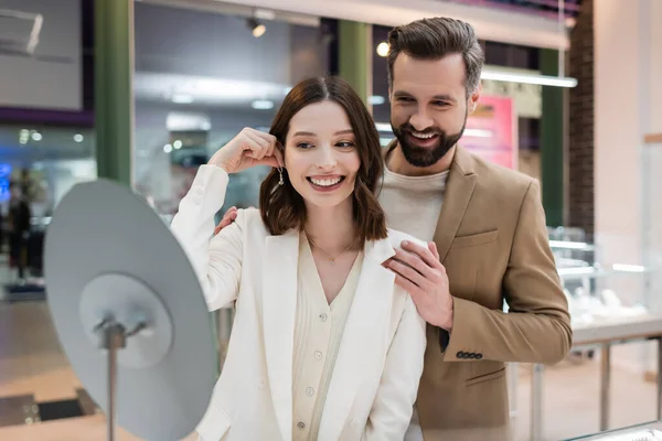 Smiling man hugging girlfriend with earring in jewelry shop