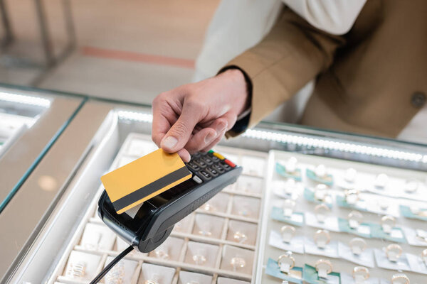 Cropped view of man paying with credit card near blurred girlfriend in jewelry shop 