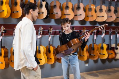 Müzik dükkanında Afrika kökenli Amerikalı bir satıcının yanında akustik gitar tutan müzisyen.