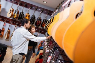 Müşteri ve Afrikalı Amerikalı satıcı müzik dükkanında akustik gitarlara bakıyor. 