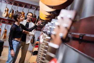 Müzik dükkanında Afrika kökenli Amerikalı bir satıcının yanında akustik gitar seçen genç bir kadın. 
