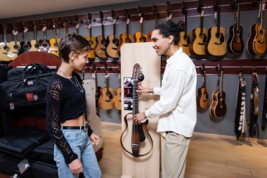 KYIV, UKRAINE - FEBRUARY 16, 2022: Side view of african american seller holding electric guitar near customer in music store 