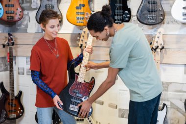 KYIV, UKRAINE - FEBRUARY 16, 2022: African american customer touching electric guitar near seller in music shop  clipart