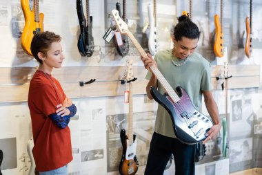 KYIV, UKRAINE - 16 Şubat 2022: Genç Afrikalı Amerikalı müşteri, müzik dükkanında elektro gitaristin yanında 