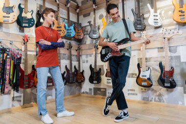 KYIV, UKRAINE - FEBRUARY 16, 2022: Seller looking at african american customer playing electric guitar in music store 