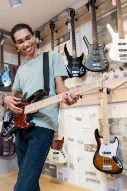 KYIV, UKRAINE - FEBRUARY 16, 2022: Smiling african american customer playing electric guitar in music store  clipart