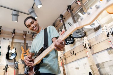 KYIV, UKRAINE - FEBRUARY 16, 2022: Low angle view of cheerful african american buyer playing electric guitar in music shop 