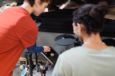 Seller standing near electronic drum set and african american customer in music store 