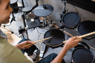 Blurred african american customer playing electronic drums in music store 