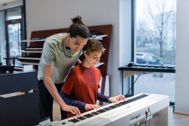 Young woman playing synthesizer with african american boyfriend in music store 