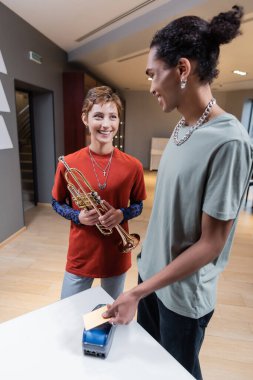 Smiling african american man paying with credit card near girlfriend with trumpet in music store 