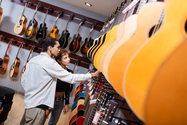 Customer and african american seller looking at acoustic guitars in music store