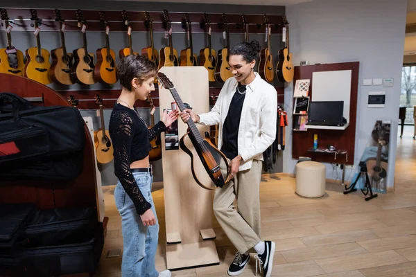 KYIV, UKRAINE - FEBRUARY 16, 2022: African american seller holding electric guitar near customer in music store 