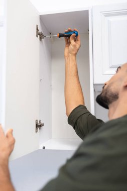 Blurred muslim man with screwdriver fixing hinge in cabinet in kitchen at home 