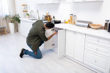 Young arabian craftsman fixing cabinet under worktop in kitchen  