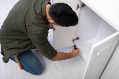 Overhead view of blurred man fixing hinge on door of kitchen cabinet 