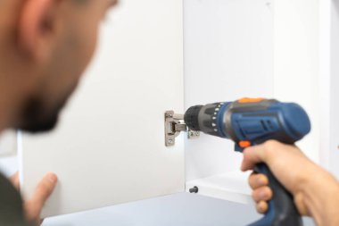 Blurred man holding electric screwdriver while fixing cupboard at home 