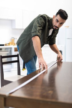Arabian carpenter measuring blurred wooden table in kitchen 