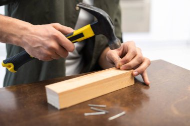 Cropped view of carpenter holding hammer near nails and wooden board 