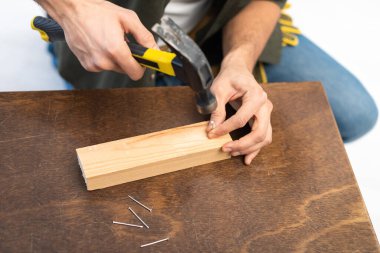 Cropped view of craftsman holding hammer and nail near wooden board on table 