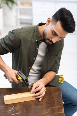 Arabian craftsman holding hammer near nails and board at home 