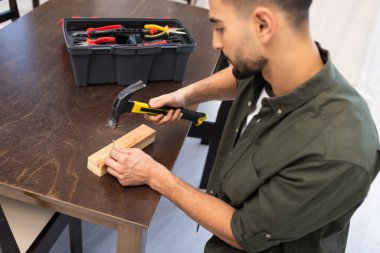 Blurred arabian carpenter holding nail and hammer near wooden board at home 