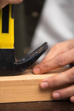 Cropped view of man picking up nail with manner near wooden board 