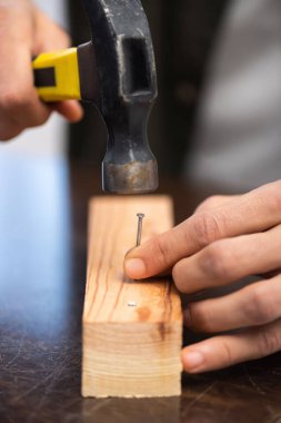 Cropped view of craftsman holding hammer and nail near wooden plank at home 