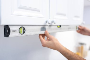 Cropped view of man holding spirit level near kitchen cabinet 