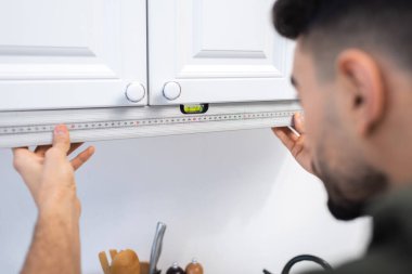 Blurred muslim craftsman measuring level of kitchen cabinet at home 