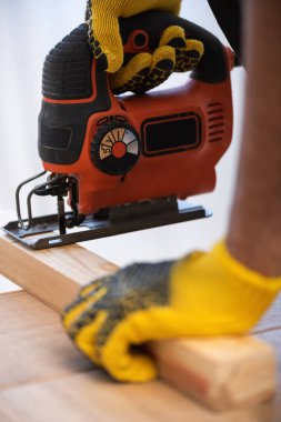 Cropped view of man in gloves sawing board at home 