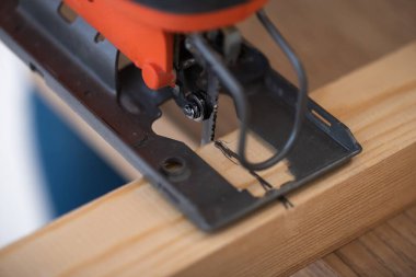Close up view of electric jigsaw machine and wooden plank 