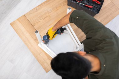 Overhead view of craftsman fixing chair with electric screwdriver near toolbox at home 