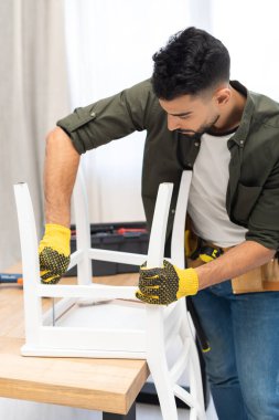 Arabian man fixing chair with screwdriver near blurred toolbox at home 