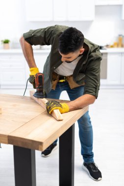 Arabian man in gloves sanding wooden board at home 