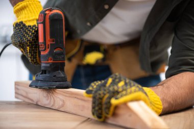 Cropped view of carpenter sanding wooden plank with tool at home  clipart