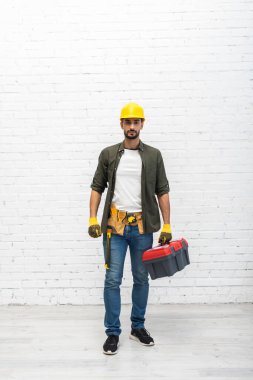 Arabian man in hardhat holding toolbox at home 