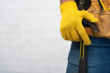 Cropped view of craftsman in glove holding hammer in tool belt at home 