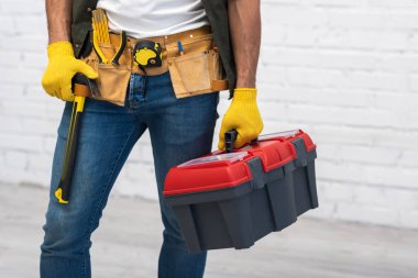 Cropped view of repairman in gloves and tool belt holding box at home 