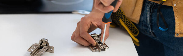 Cropped view of man with tool belt fixing hinge of cupboard, banner 