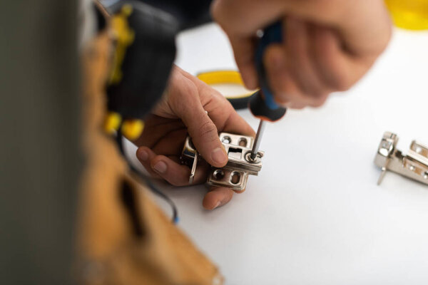 Partial view of blurred craftsman fixing hinge of cabinet at home 