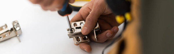 Cropped view of man screwing nail from hinge of cupboard at home, banner 