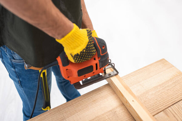 Высокоугольный вид человека, держащего электропилу возле деревянной доски у себя дома 