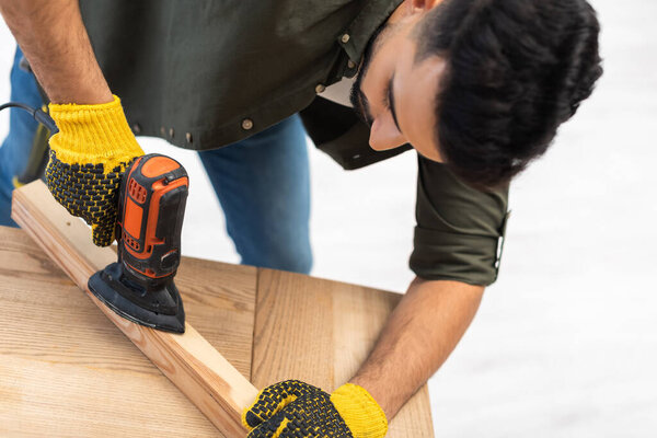 Arabian carpenter sanding wooden board with electric sander at home 