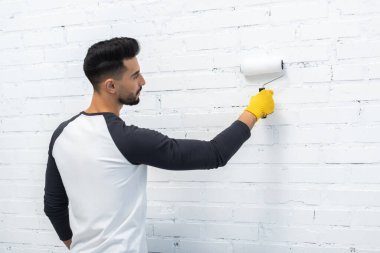Side view of muslim man in glove coloring brick wall at home 